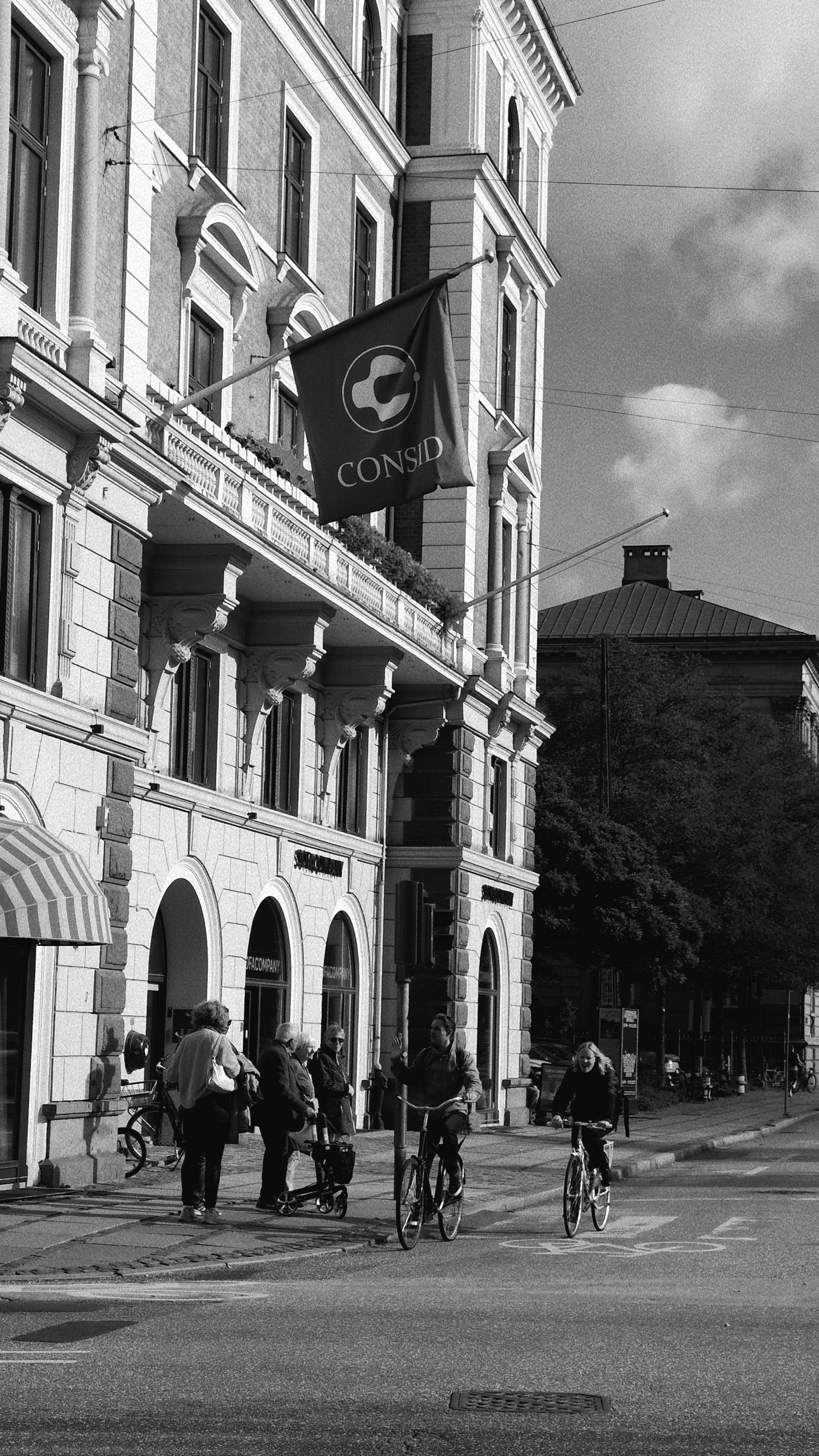 Black and white photo of cyclists passing by Consid building in Copenhagen, Denmark.