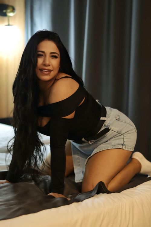 Free A confident young woman poses indoors in a stylish outfit with denim shorts and a black top. Stock Photo