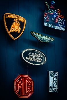 Vibrant neon signs showcasing luxury vehicle brands and logos in a dark, moody setting.
