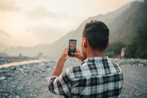 Free Man takes a photo of a scenic mountain landscape with his smartphone during sunset. Stock Photo