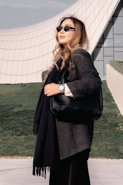 Free Fashionable woman in sunglasses and coat stands confidently by modern architecture. Stock Photo