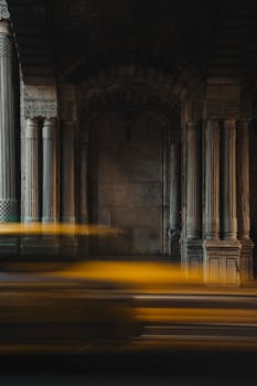 Yellow taxi moving past ancient stone columns, showcasing motion blur effect.