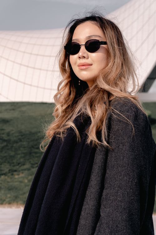 Free Portrait of a fashionable woman with sunglasses outdoors near a modern architectural structure. Stock Photo