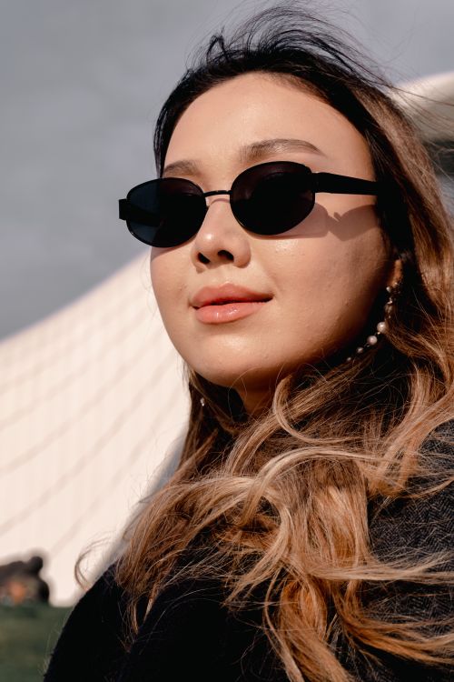 Free Trendy young woman in sunglasses posing with a bright smile against a modern architectural backdrop. Stock Photo