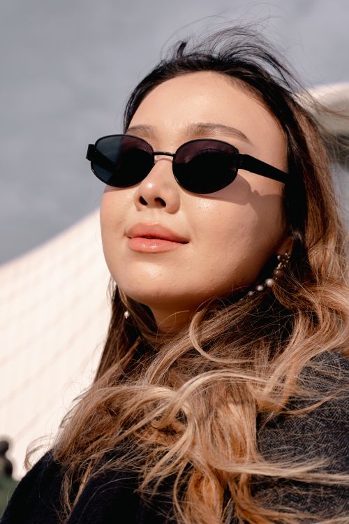 Free Confident woman wearing chic sunglasses, posing in front of modern architecture. Stock Photo