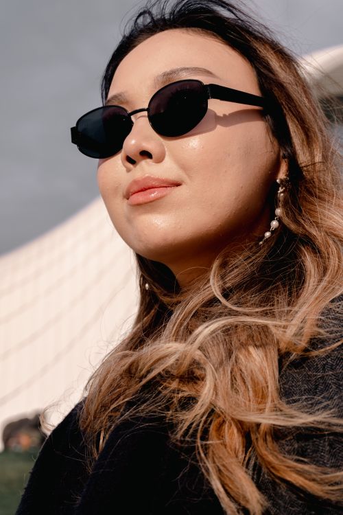 Free Close-up of a stylish woman wearing sunglasses and jewelry with a modern architectural background. Stock Photo