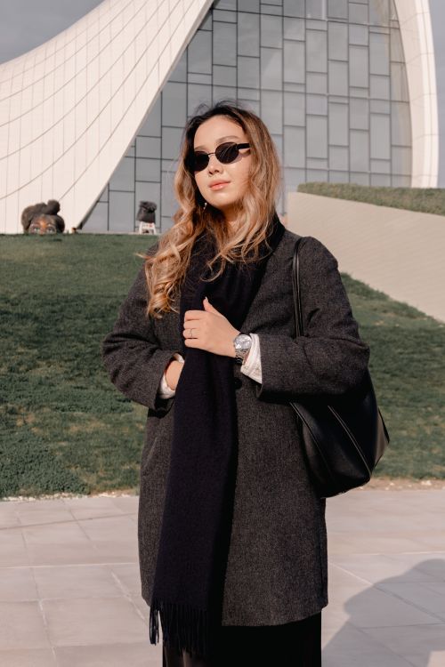 Free Confident woman in sunglasses and coat standing in front of a unique architectural structure. Stock Photo