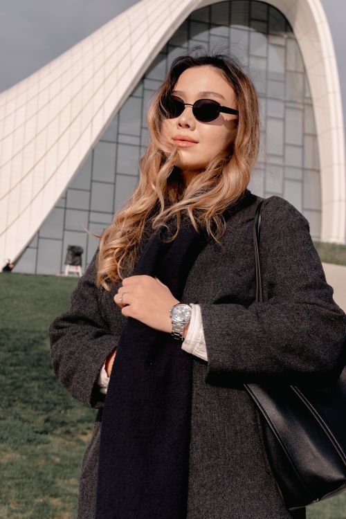 Free Confident woman in sunglasses poses before modern curved architecture under sunny skies. Stock Photo