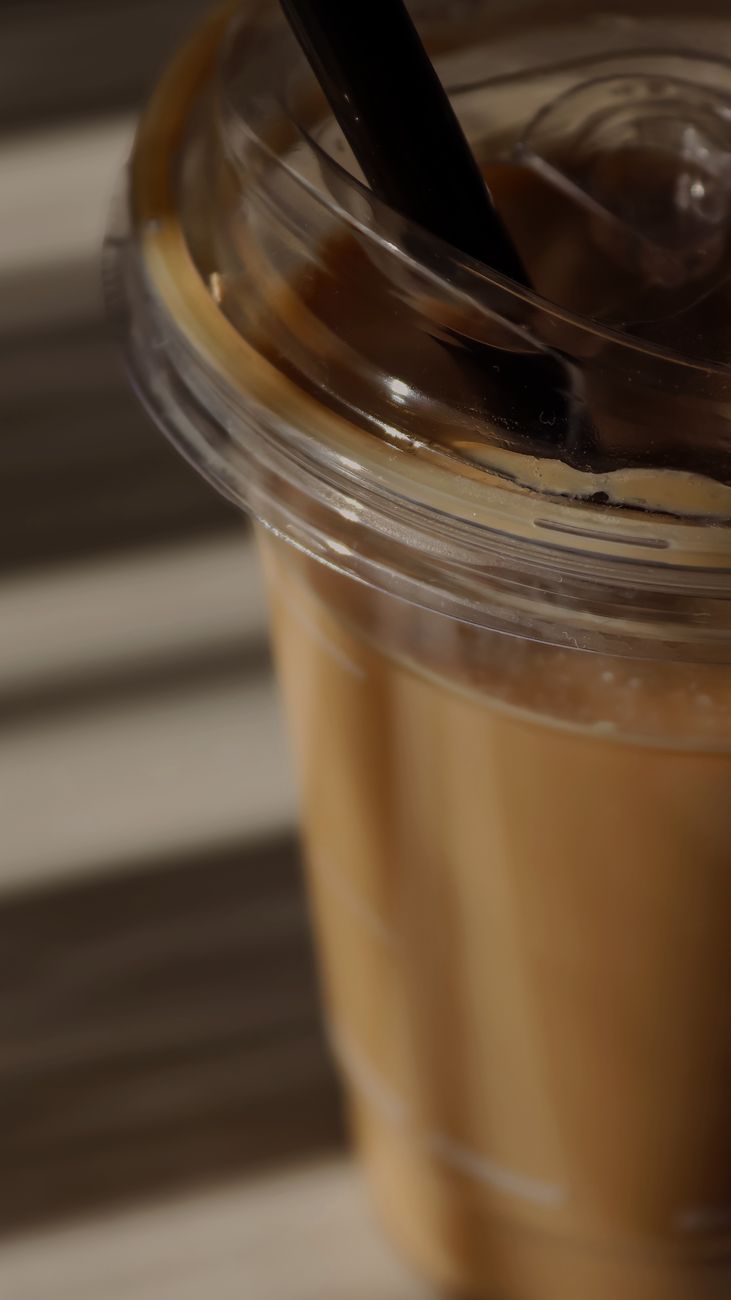 Refreshing iced coffee in a clear plastic cup with a straw on a striped surface.