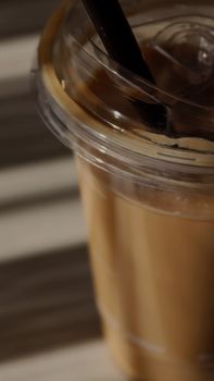 Refreshing iced coffee in a clear plastic cup with a straw on a striped surface.