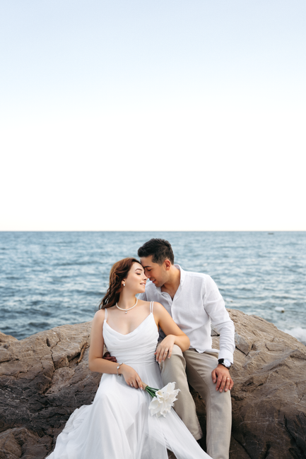 Bride and groom share a romantic moment on rocky Antalya beach with the ocean as a backdrop.