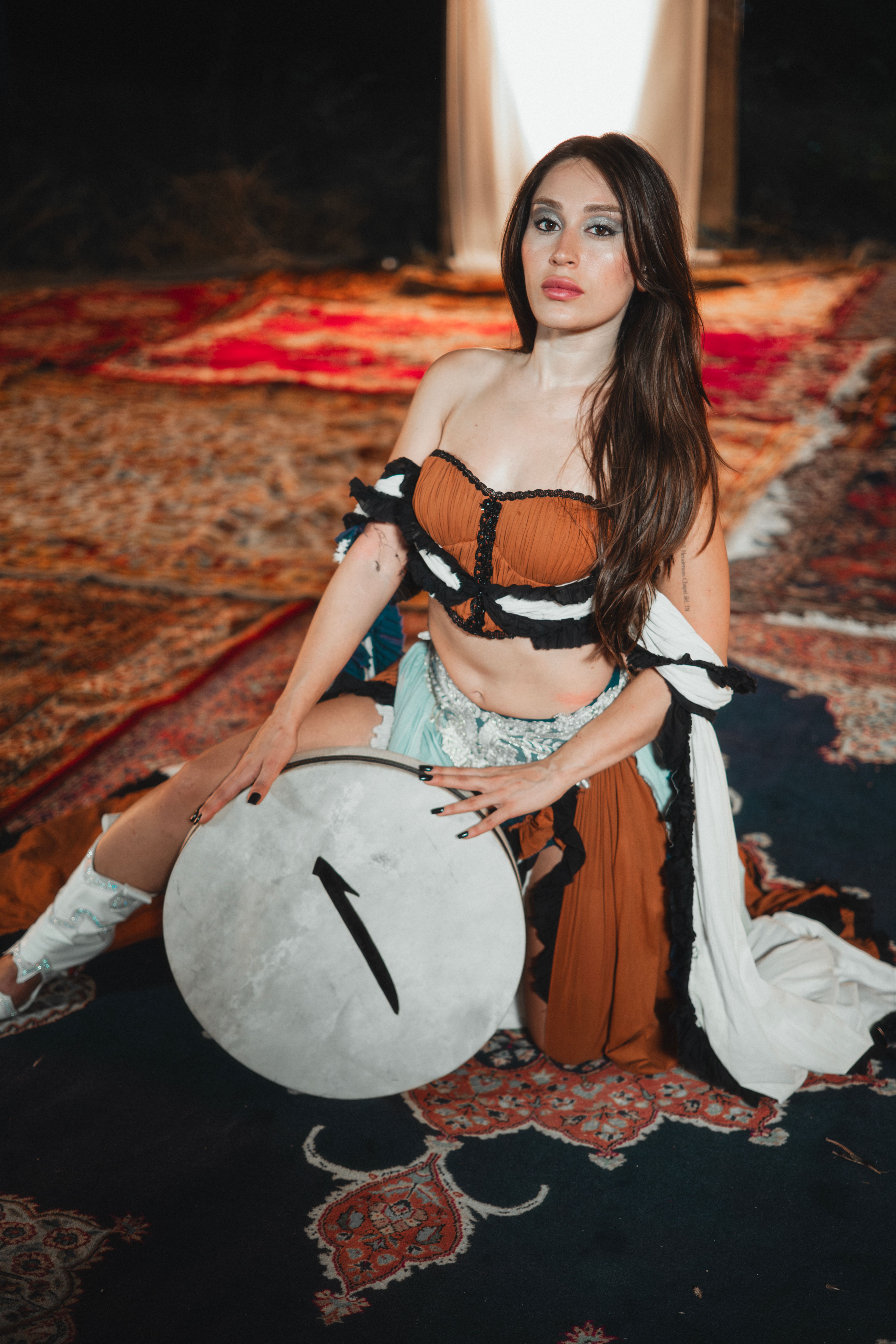 Captivating woman in colorful attire gracefully holding a traditional drum, creating an exotic and artistic ambience.