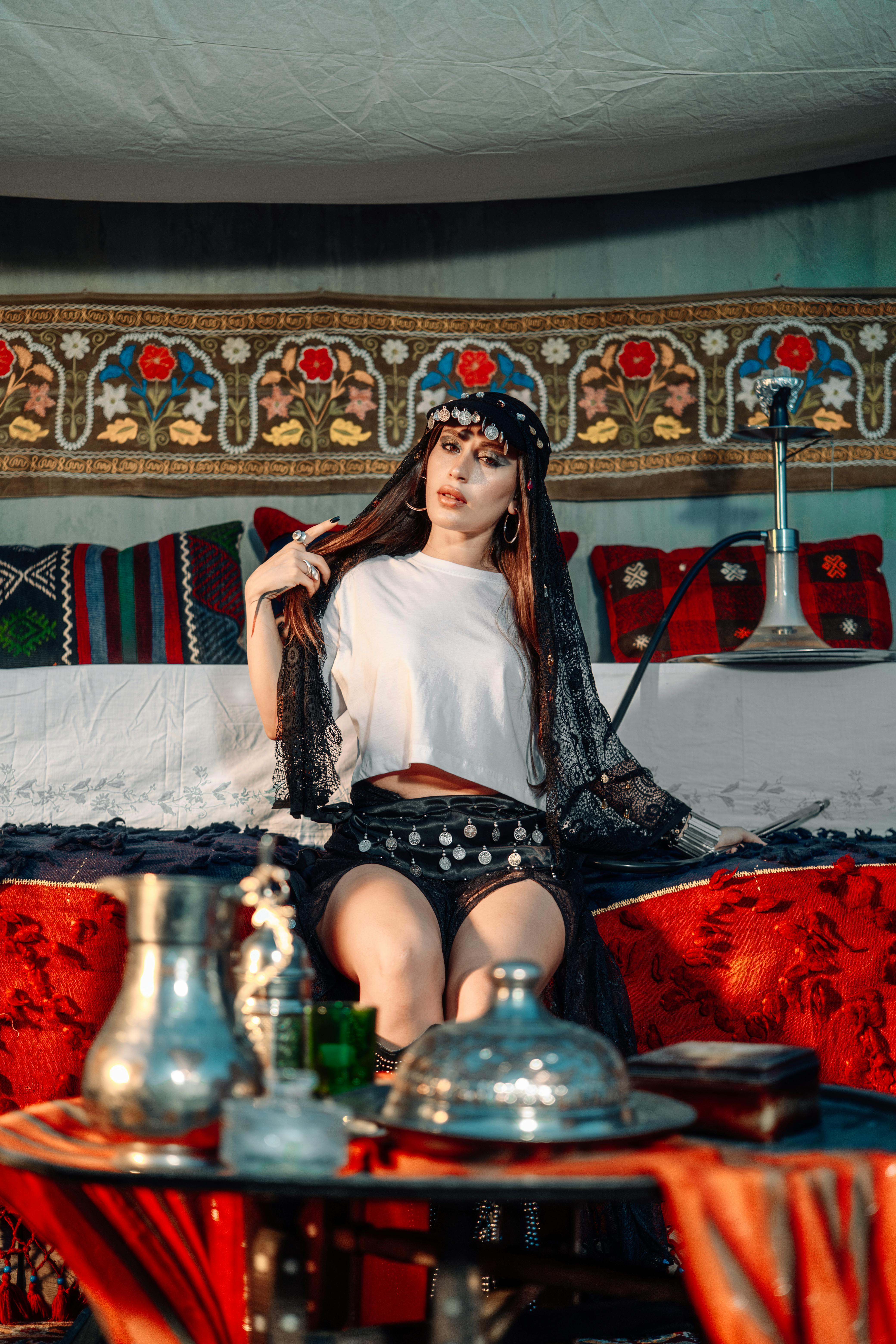 A woman in traditional attire poses indoors amidst vibrant Middle Eastern decor.