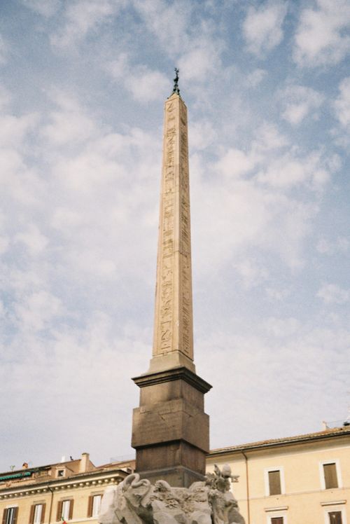 Free View of the towering Egyptian obelisk in Piazza Navona, Rome, under a blue sky. Stock Photo
