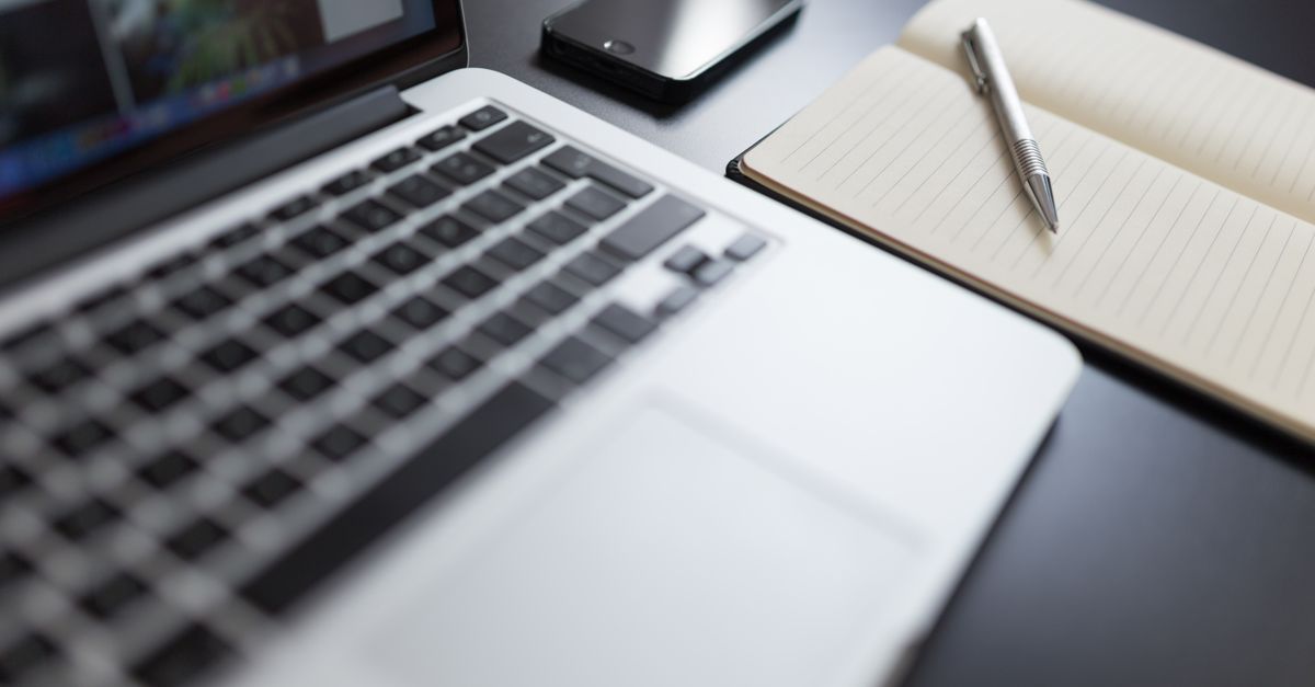 Un espacio de trabajo moderno con un laptop, cuaderno, smartphone y bolígrafo en un escritorio.