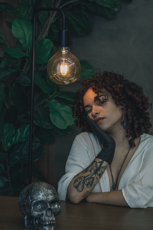 Free Dark moody portrait of a woman with tattoos, under intimate lighting with a decorative skull. Stock Photo