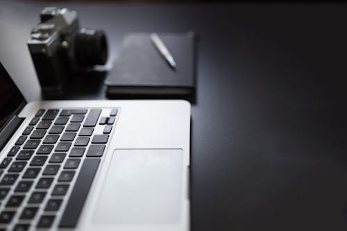 Grayscale Photography of Laptop Computer Beside Book and Camera