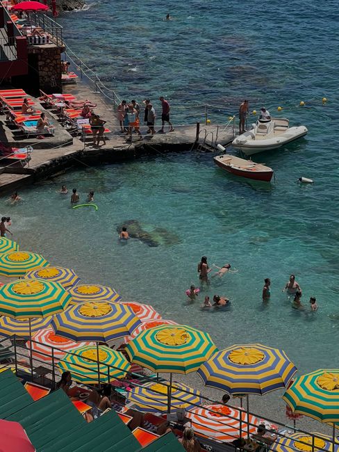 Lively beach view with colorful umbrellas and people enjoying the water in Positano, Italy.