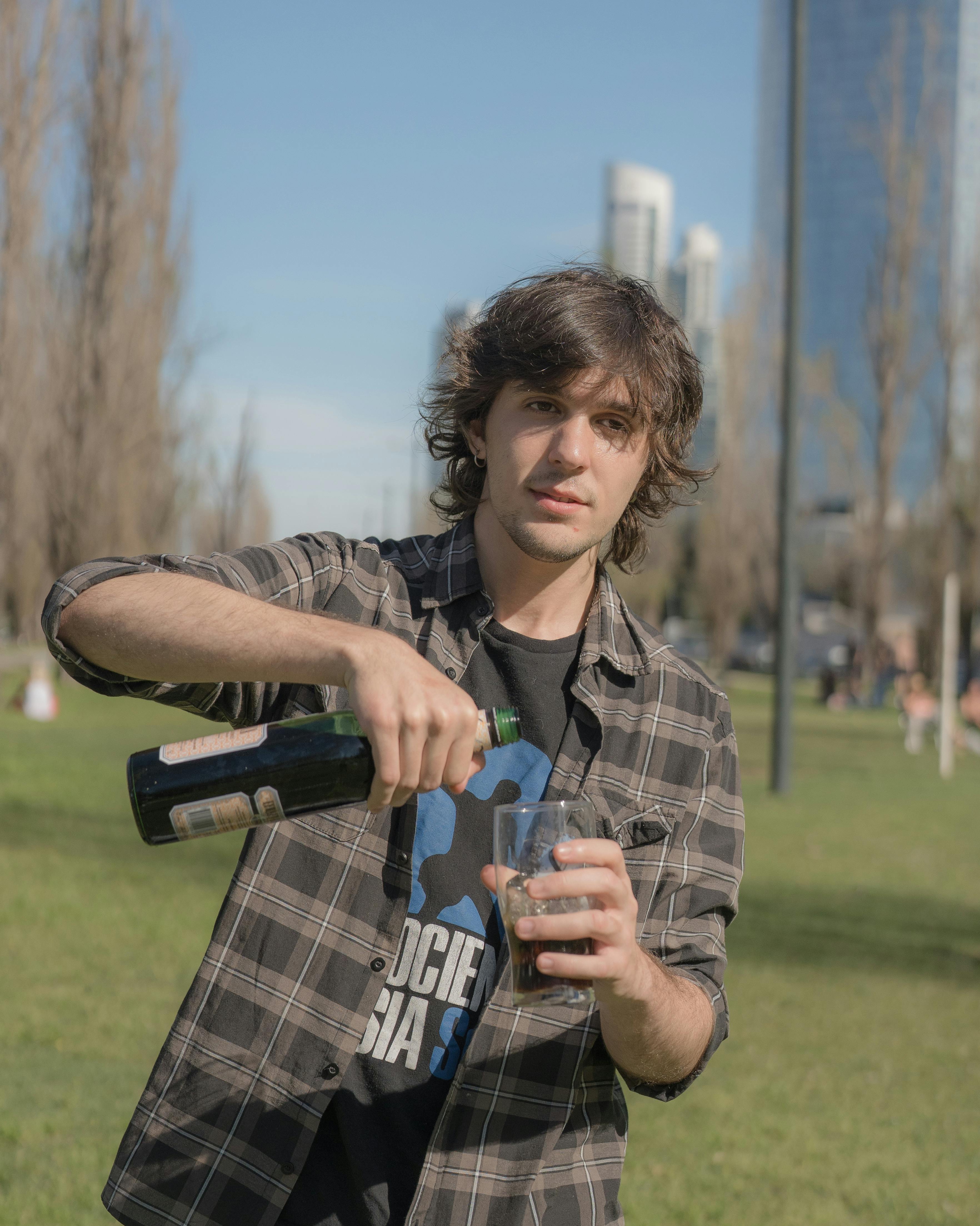 A young man pours a drink in a park with Buenos Aires skyline in the background.