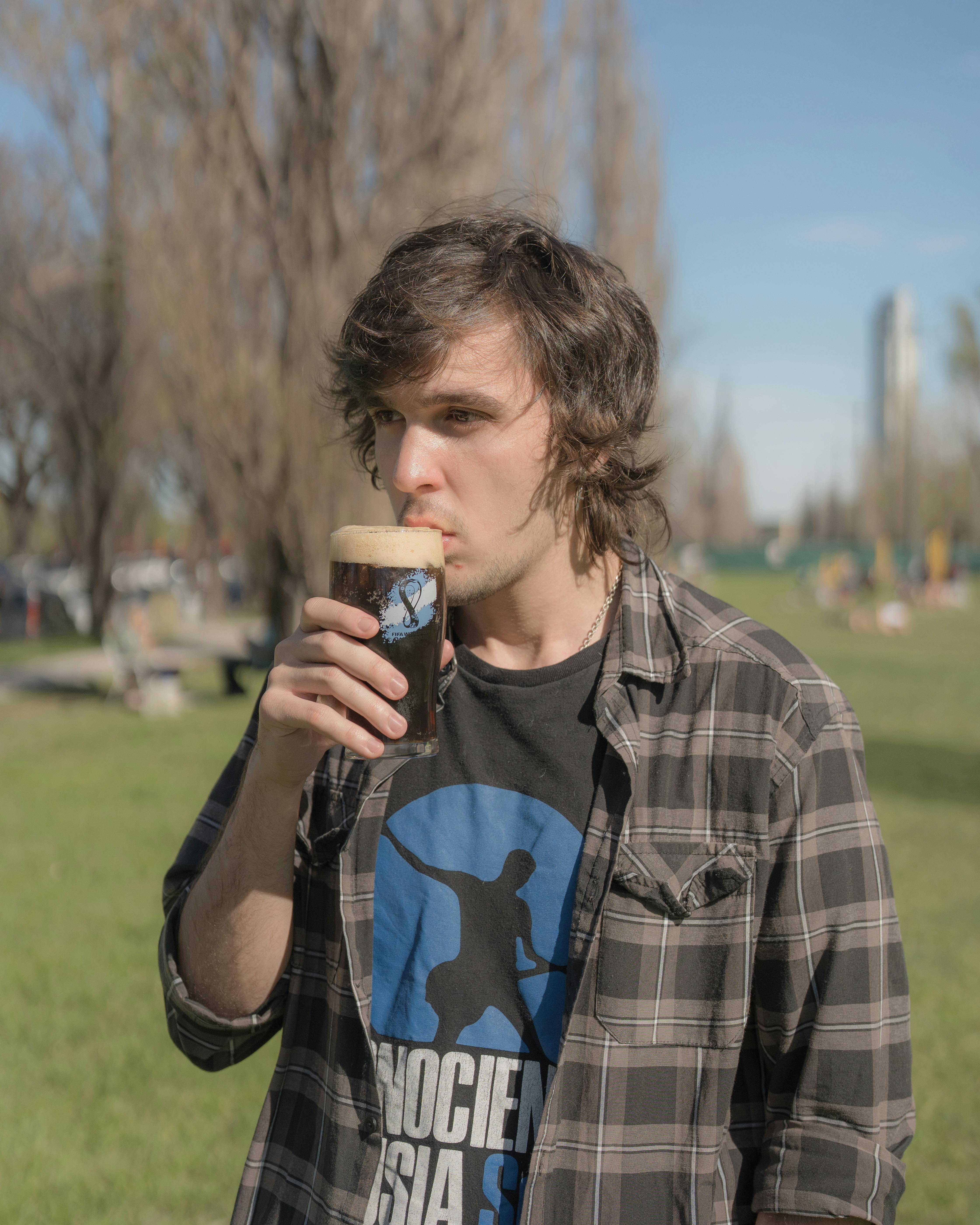 A young man drinking a stout beer in a sunny Buenos Aires park, enjoying a relaxing day outdoors.