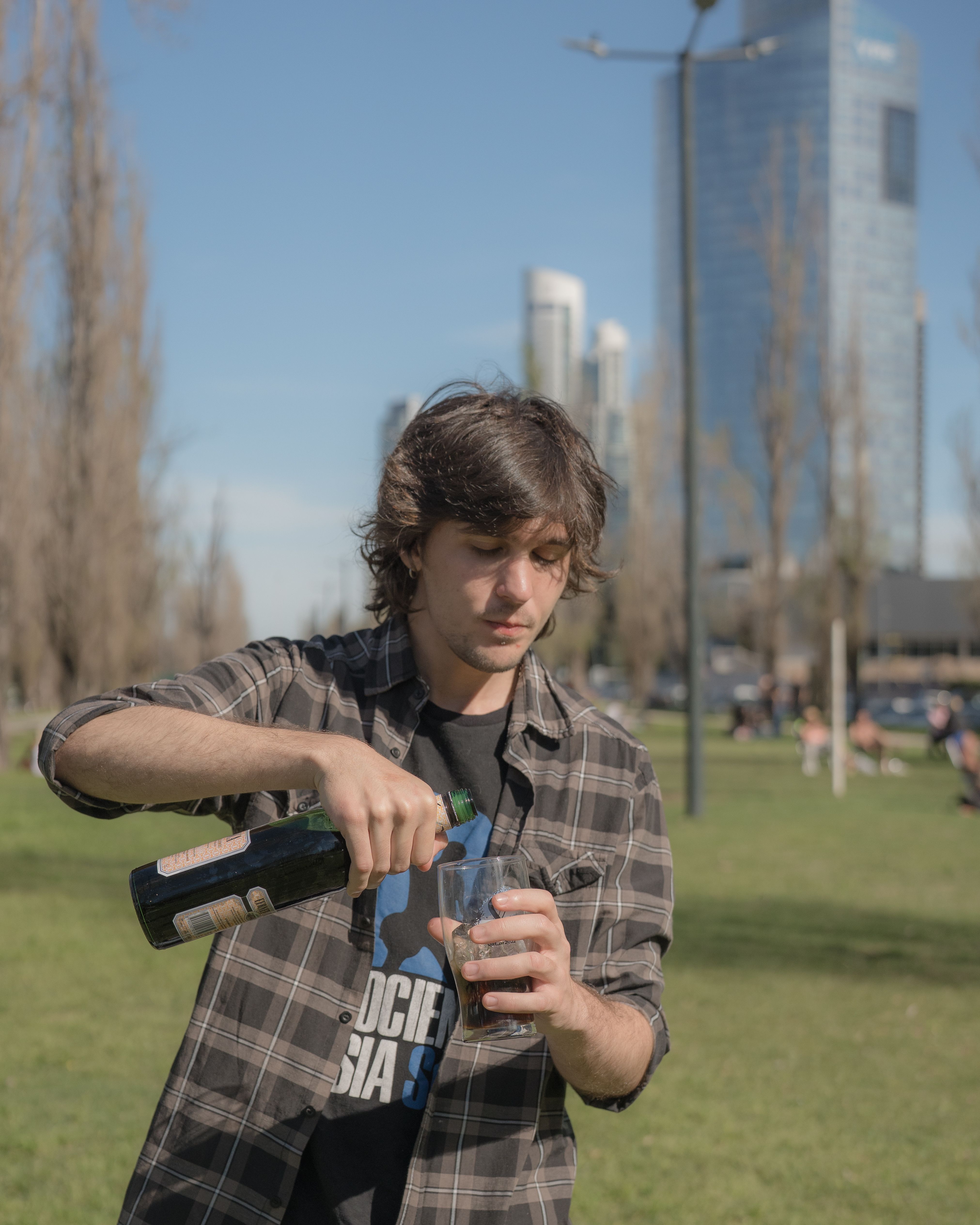A young man pours a drink outdoors in Buenos Aires with city skyline in background.