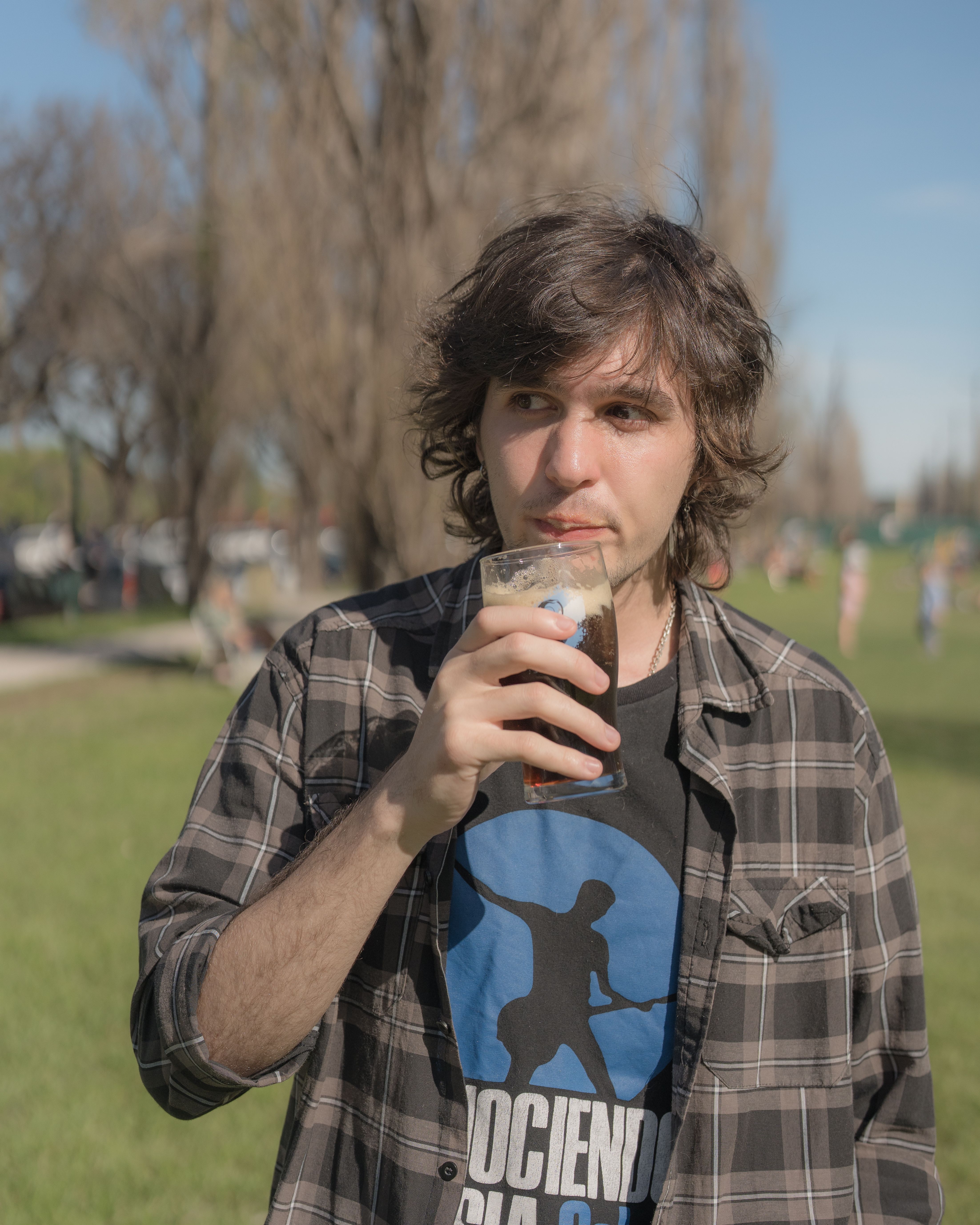 Young man enjoying a drink outdoors in a Buenos Aires park under a bright sun.