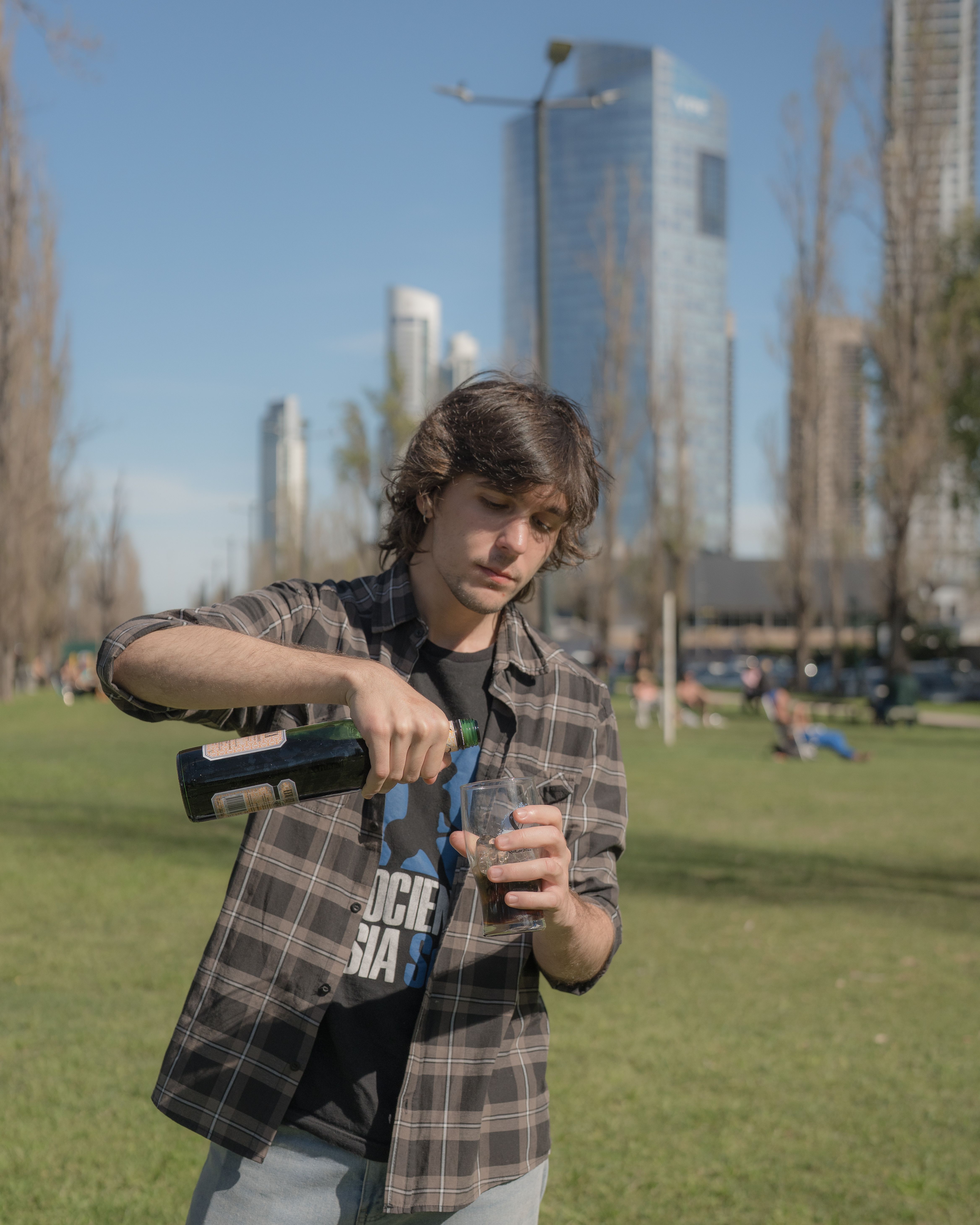 A young man pours maté in a park in Buenos Aires with skyscrapers in the background.