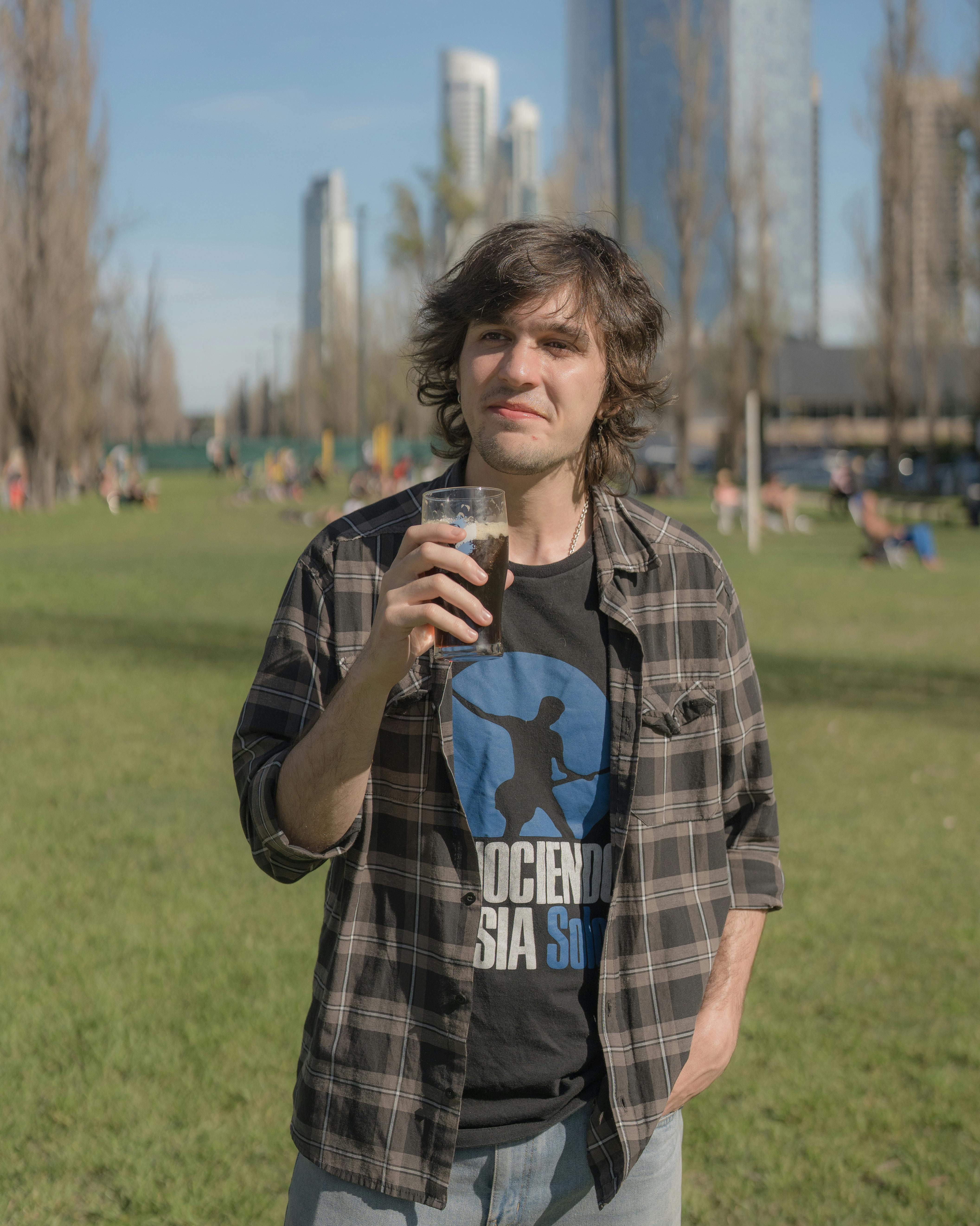 Casual portrait of a man enjoying a drink in a sunny Buenos Aires park setting.