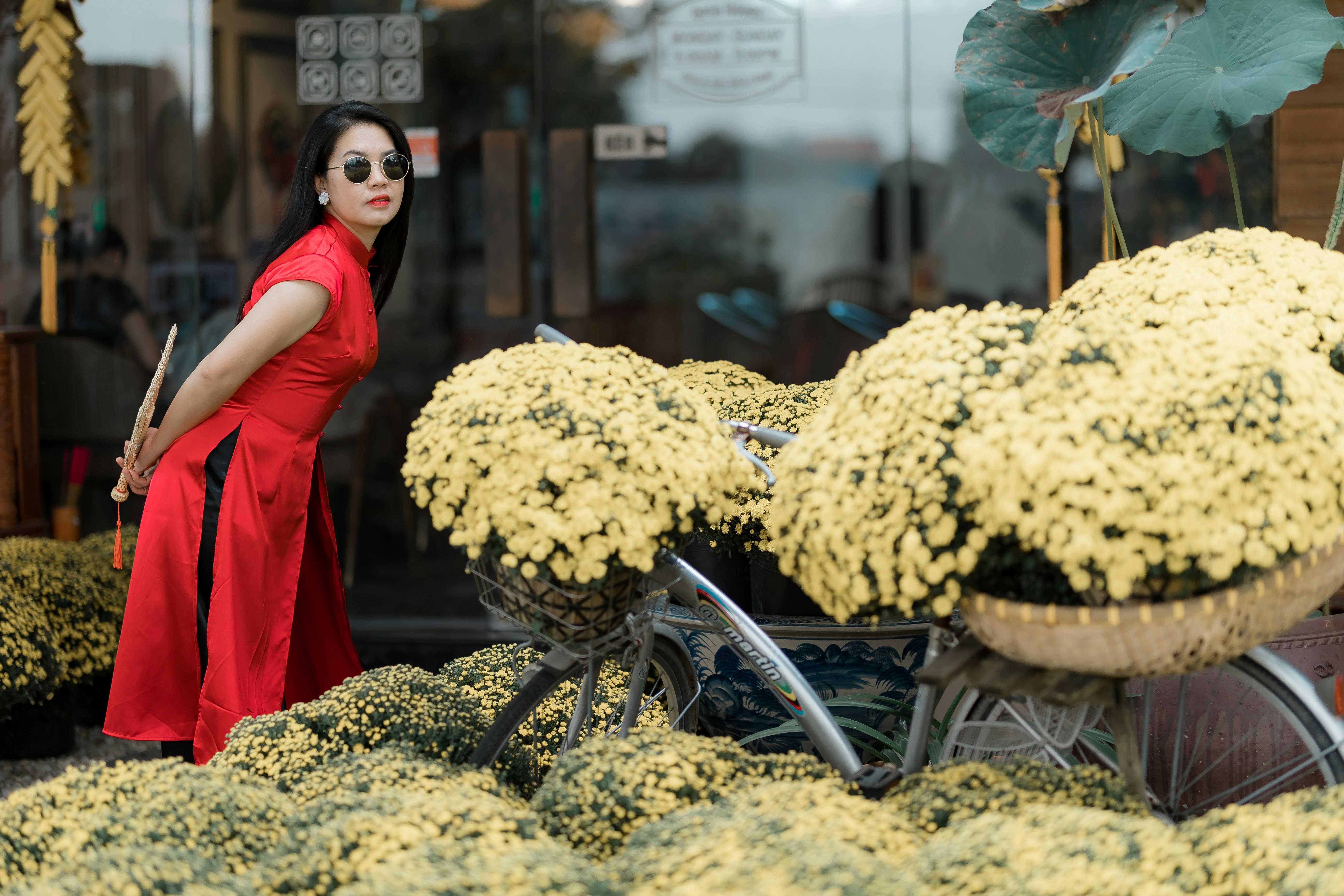 一位时尚女士推着一辆装饰着黄色花朵的自行车，正在摆姿势