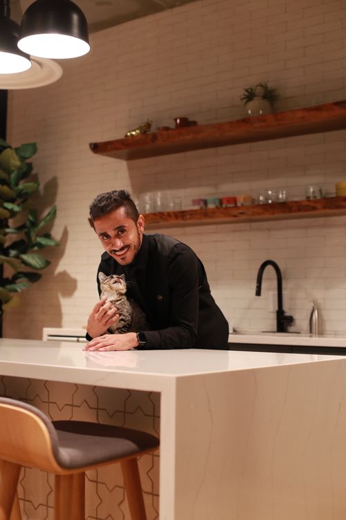 Free A man smiling while holding a cat in a stylish kitchen with underlit counters. Stock Photo