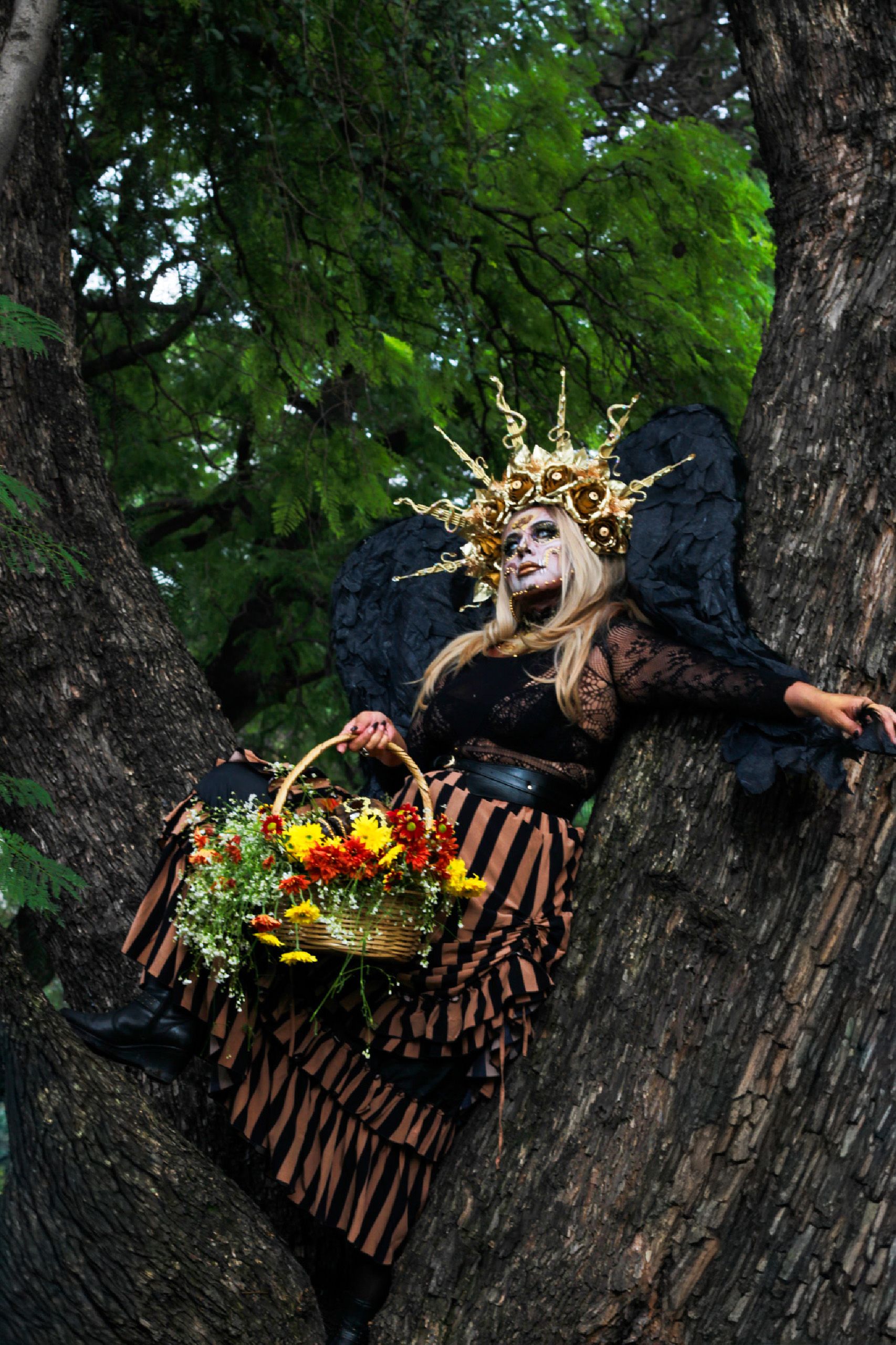 A captivating portrait of a person in elaborate costume and makeup, perched in a tree with a basket of flowers.