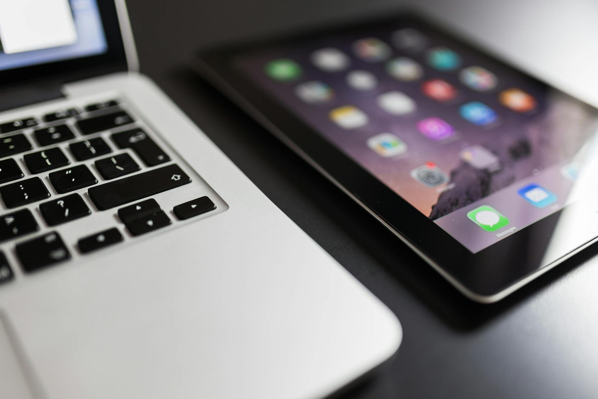 Close-up of a laptop and tablet on a black desk, showcasing modern technology essentials.