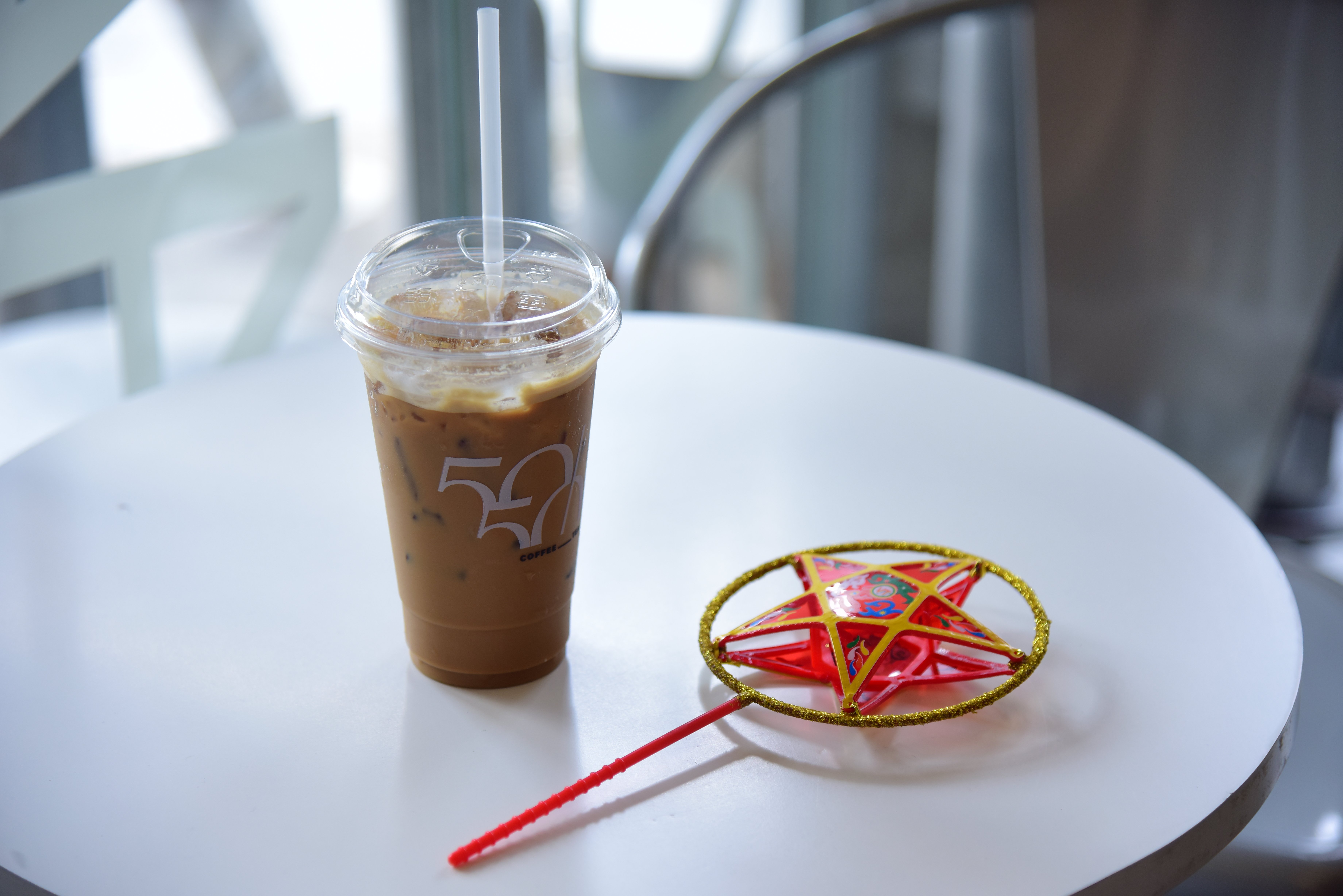 Iced coffee with straw and red star lantern on modern round cafe table indoors.