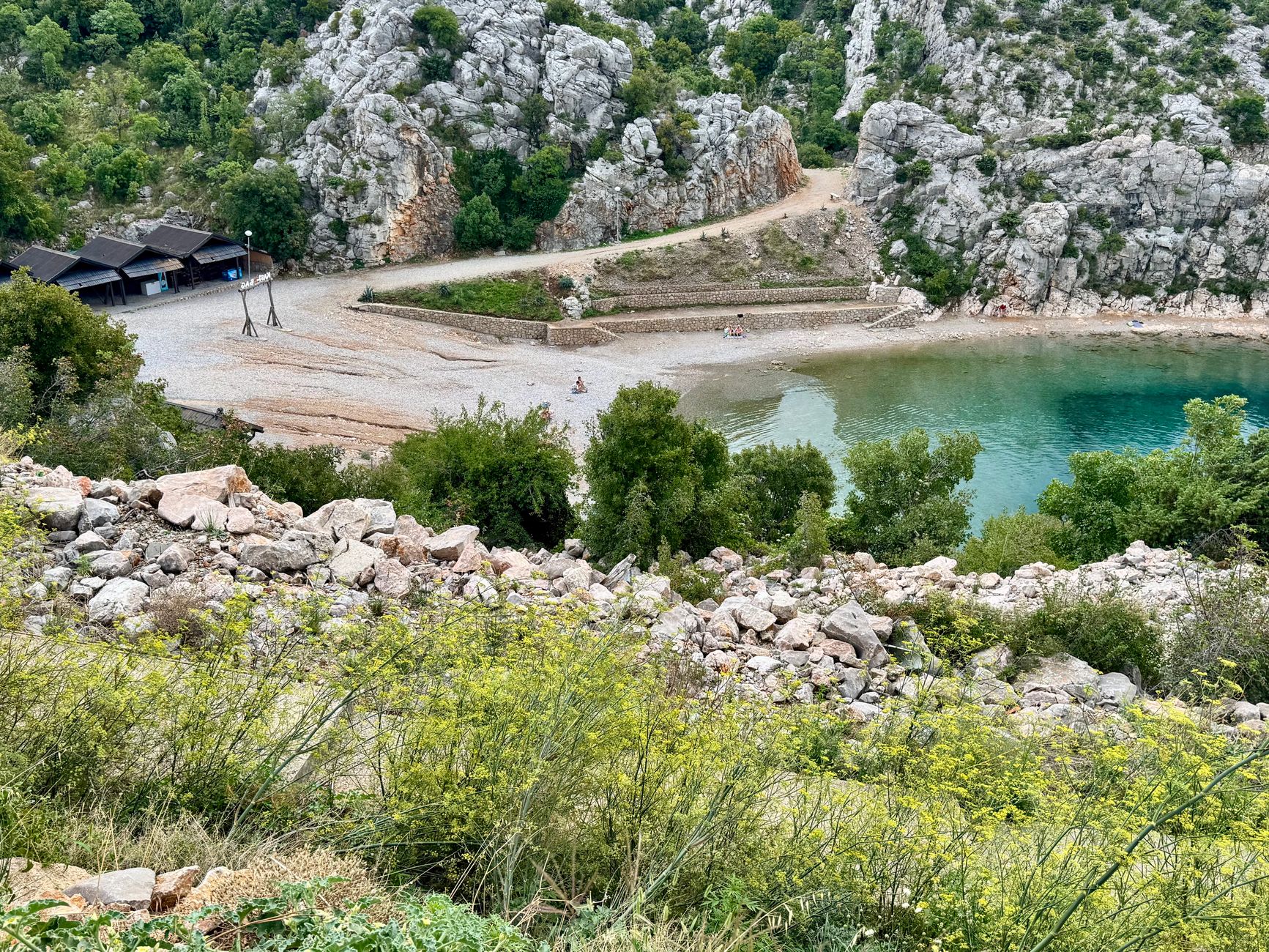 Discover the serene beach cove in Karlobag, Croatia surrounded by lush greenery and rocky cliffs.