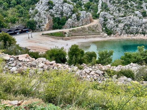 Discover the serene beach cove in Karlobag, Croatia surrounded by lush greenery and rocky cliffs.