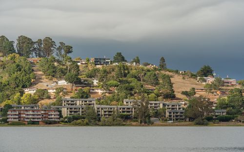 Free Hillside homes overlook a serene lake under a cloudy sky, offering a picturesque landscape. Stock Photo