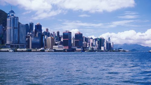 Free Vibrant Hong Kong skyline viewed across Victoria Harbour on a sunny day. Stock Photo