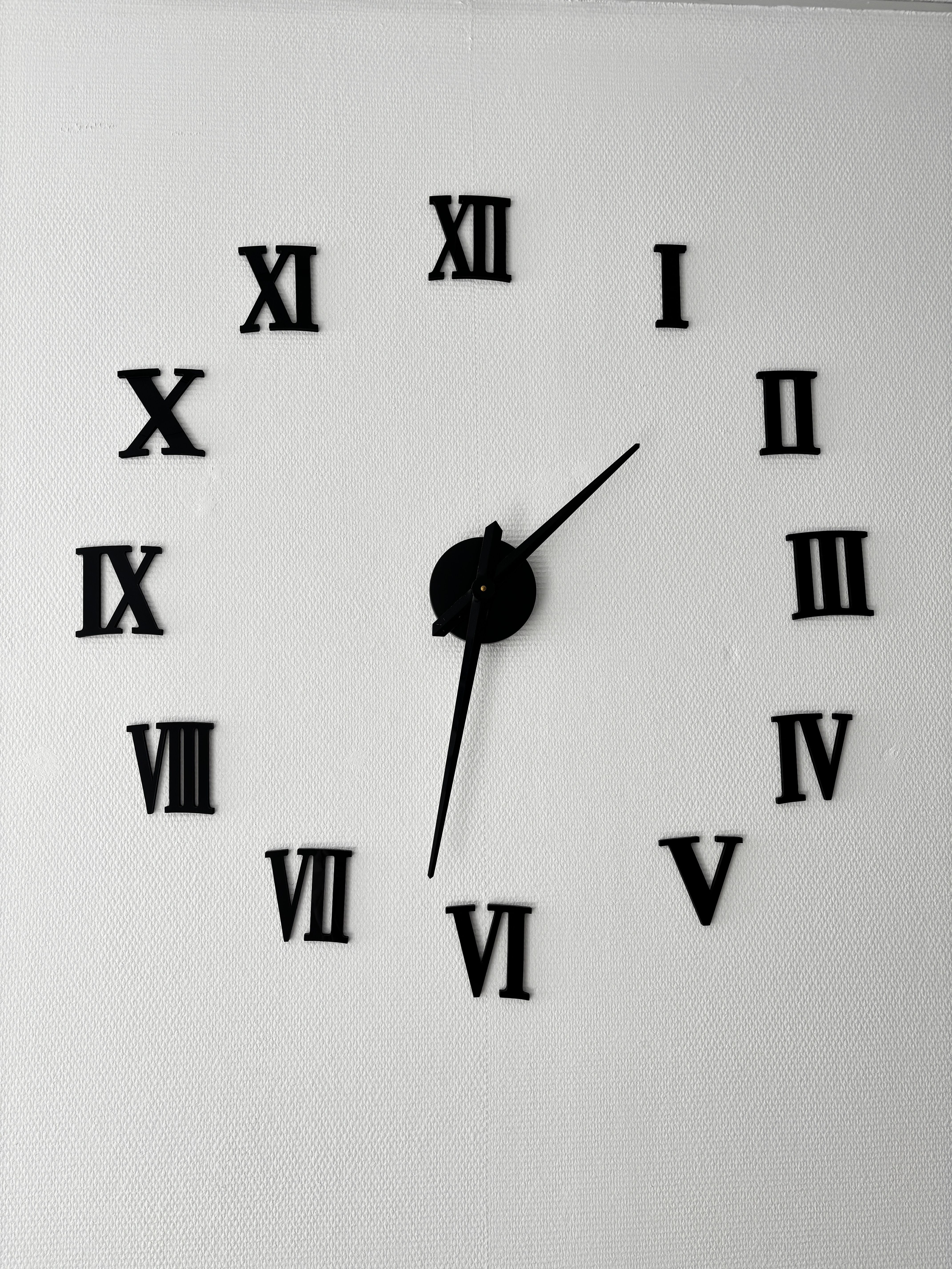 Minimalist wall clock with Roman numerals against a textured white background, simple design.