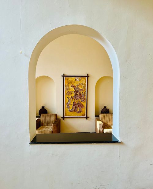 Free A rustic seating area with traditional Indian artwork in a serene setting, captured through an archway. Stock Photo