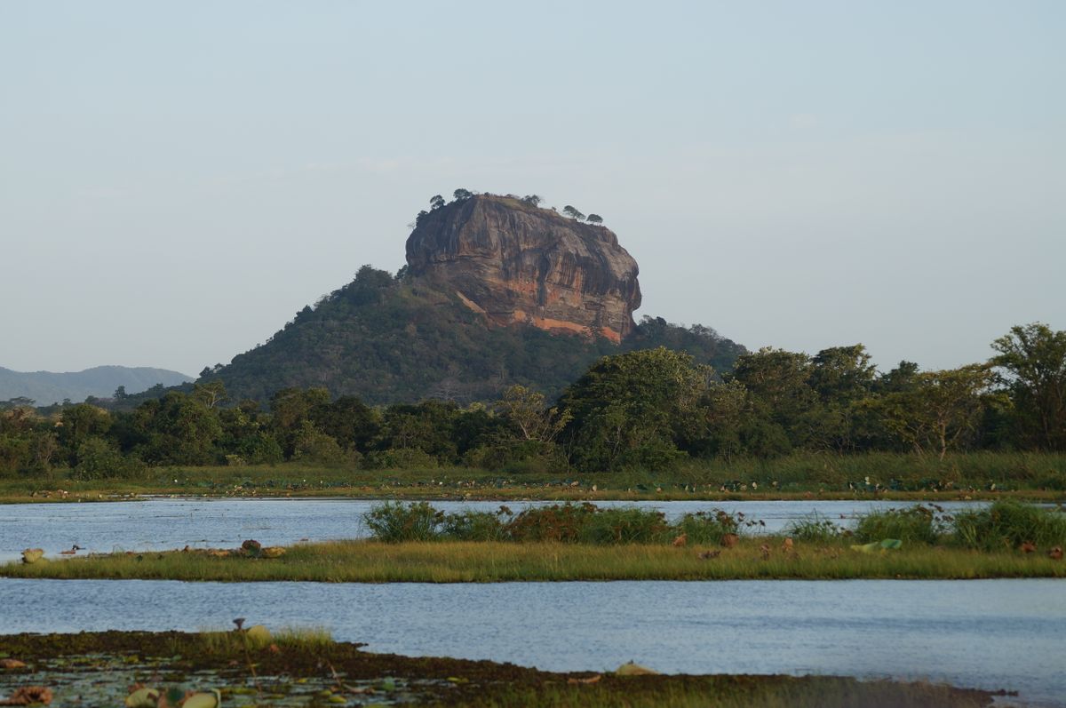 Sigiriya rock fortress rising from jungle beside still water