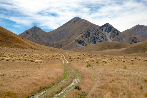 Free Explore the rugged beauty of Lindis Pass, New Zealand with a dirt trail leading to majestic mountains. Stock Photo