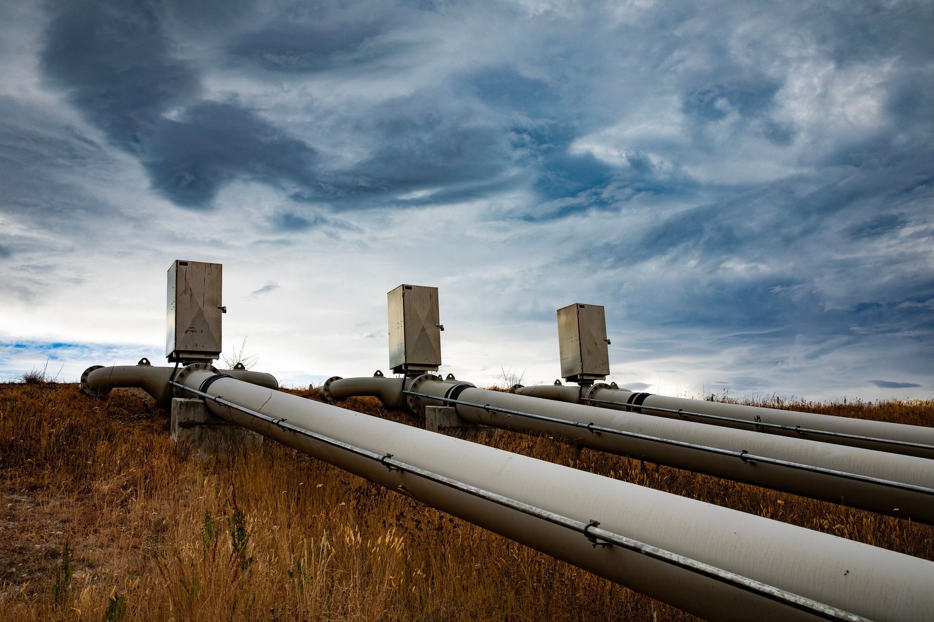 A series of large industrial pipes under a dramatic cloudy sky in New Zealand.