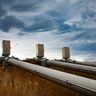 Large industrial pipelines with control valves stretching across a dry landscape under a dark, dramatic sky.
