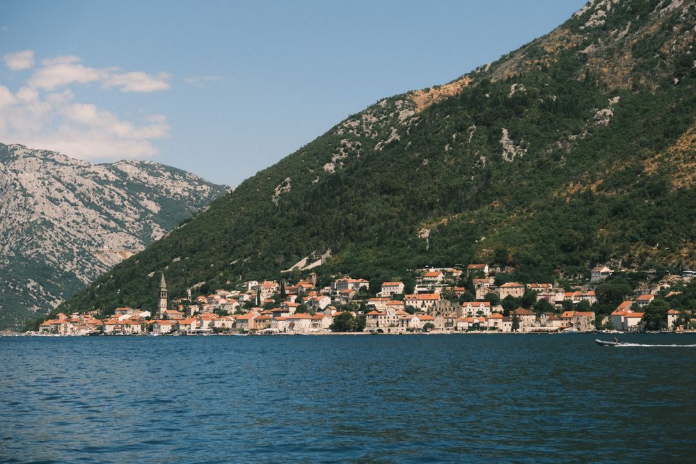 Orășelul baroc Perast văzut de peste apă, cu campanil și munți