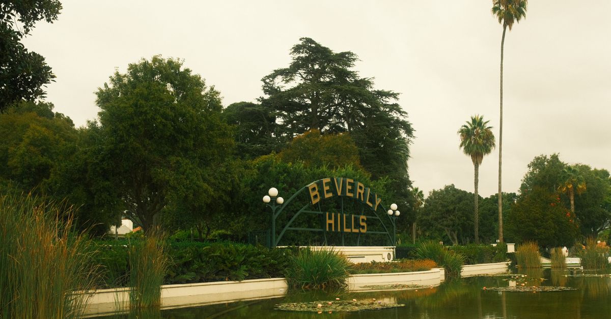 Tranquil Beverly Hills sign by a lush pond with palm trees on a cloudy day.