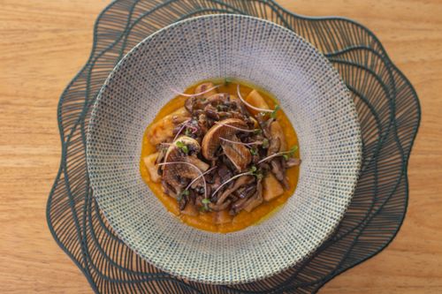 Free Delicious gourmet mushroom dish served in a textured bowl on a wooden table. Stock Photo