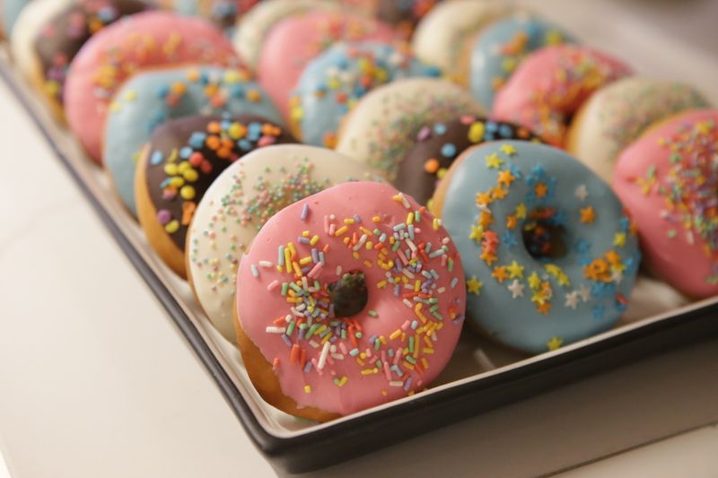 Tray of doughnuts with colourful icing and sprinkles, photo by Fernanda da Silva Lopes on Pexels