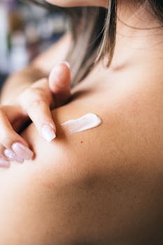 A woman applies creamy moisturizer to her shoulder, focusing on skincare and wellness.