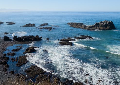 Stunning rocky coastline with waves crashing on rocks under a clear blue sky.