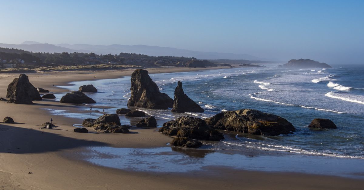 Explore the stunning rock formations and waves at Bandon Beach, Oregon under a clear blue sky.